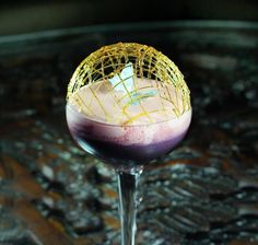 a purple drink in a wine glass with gold garnish