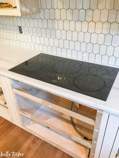 a stove top sitting inside of a kitchen next to a wooden floor and white cabinets