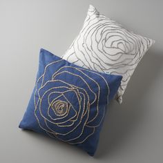 two blue and white pillows on a gray surface with gold threadwork in the middle