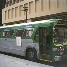 a green and white bus parked in front of a tall building next to a sidewalk