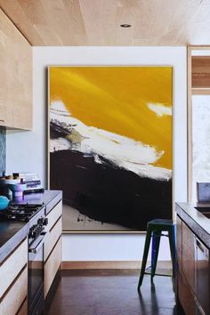 an abstract painting hangs on the wall in a kitchen with wooden cabinets and countertops