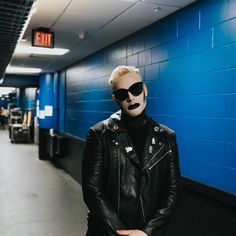 a man in black leather jacket and sunglasses standing next to blue wall