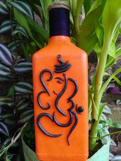 an orange and black bottle sitting next to some plants