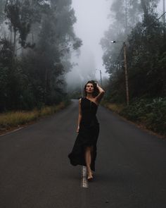 a woman in a black dress is walking down the road on a foggy day