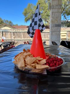 a plate with chips, raspberries and strawberries next to a cone shaped flag