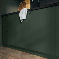 a green kitchen with black counter tops and wooden flooring on the wall, under a sink