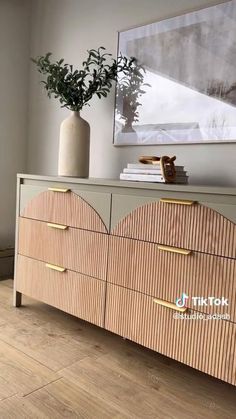 a wooden dresser with drawers and a vase on it's sideboard in front of a painting