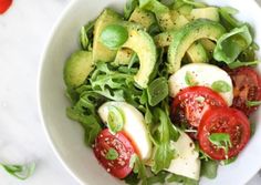 a white bowl filled with lettuce, tomatoes and sliced avocado slices