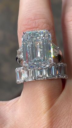 a woman's hand holding an emerald and baguette diamond ring with two side stones