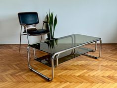 a glass table with two chairs and a potted plant on it in front of a white wall