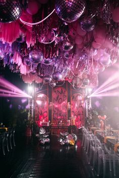 a room filled with lots of purple and pink balloons hanging from the ceiling over tables