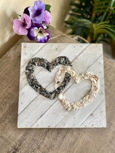 two hearts made out of seashells sitting on top of a piece of wood