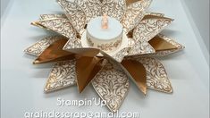 a candle sits in the center of a decorative paper flower ornament that is gold and white