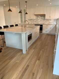 an empty kitchen with white cabinets and wood flooring is pictured in this image, the island has two stools on it