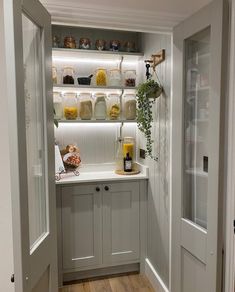 a kitchen with white cabinets and shelves filled with jars on the wall next to an open door