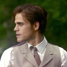 a man in a suit and tie looking off into the distance with trees in the background