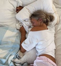 a woman laying in bed with her dog sleeping next to her on top of pillows