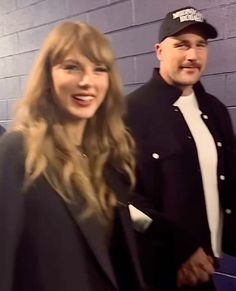 two people standing next to each other in front of a brick wall and wearing hats