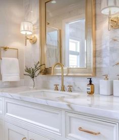 a white bathroom with gold accents and marble counter tops, along with two sinks on both sides