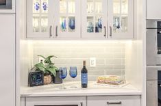 a kitchen with white cabinets and glass shelves on the wall, along with wine glasses