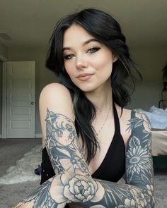 a woman with tattoos on her arms and arm is sitting in front of a bed