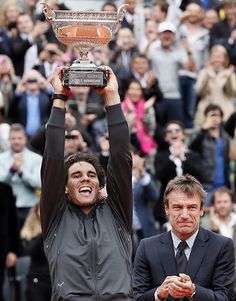 a woman holding up a tennis trophy in front of a man on the sidelines