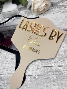 a mirror with the words lashes by on it next to some flowers and other items