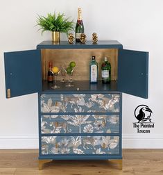 a cabinet with bottles and glasses on top of it in front of a white wall