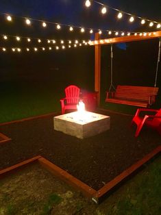 a fire pit in the middle of a yard with red chairs around it and string lights hanging above