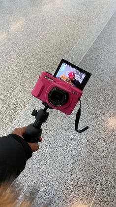 a person holding a camera up to take a picture on the ground with it's pink case