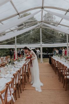 a bride and groom standing at the end of a long table in a large tent