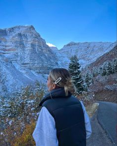 a woman standing on the side of a road looking at mountains