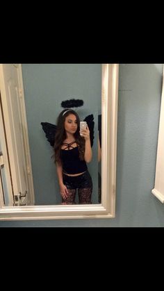 a woman taking a selfie in front of a mirror with an angel wings on her head