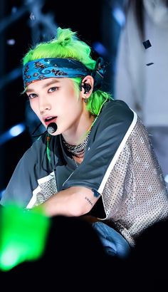 a man with green hair and piercings on his head sitting in front of a microphone