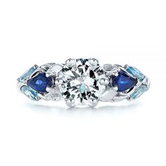 a white gold ring with blue stones and leaves on the band, set in 18k white gold