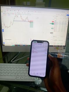 a person holding up an iphone in front of a computer screen with a stock chart on it