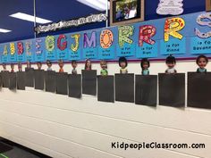 a classroom wall with posters on it and children's faces hanging from the bulletin board