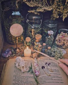 an open book sitting on top of a wooden table next to jars filled with flowers