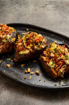 three baked potatoes with toppings on a black plate