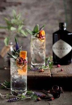 two glasses filled with different types of drinks and garnished with orange slices, herbs and flowers