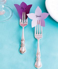 two forks with flowers on them sitting next to each other near plates and utensils