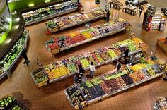 an overhead view of a grocery store filled with fruits and veggies as people shop in the produce section