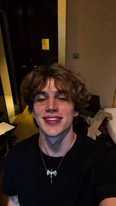 a young man with curly hair wearing a black t - shirt and smiling at the camera