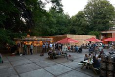 people sitting and standing around tables with red umbrellas