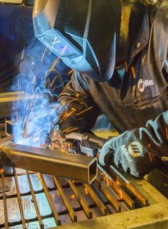 welder working on an item with sparks coming out of the welding holes in front of him