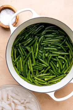 green beans are being cooked in a pot with salt and sugar on the table next to it