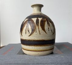 a brown and white vase sitting on top of a gray tablecloth covered bookcase