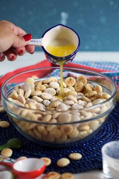 a person pouring peanut butter into a bowl of peanuts on top of a blue place mat