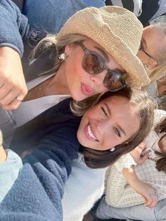 two women taking a selfie in front of a group of people wearing hats and sunglasses