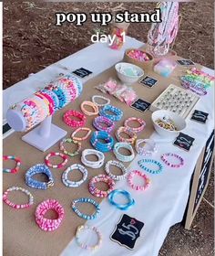 a table topped with lots of bracelets next to a sign that says pop up stand day